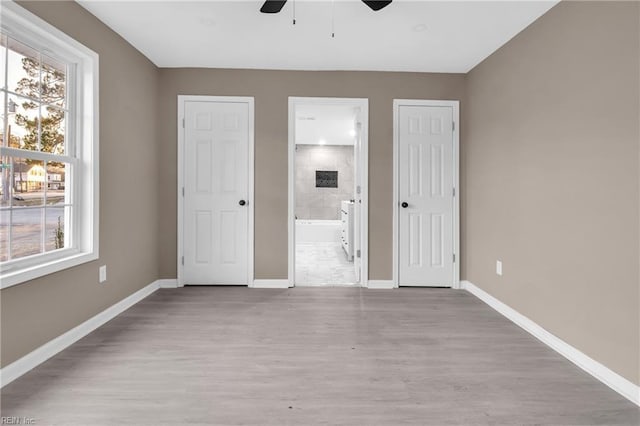 unfurnished bedroom featuring ensuite bath, wood finished floors, baseboards, and ceiling fan