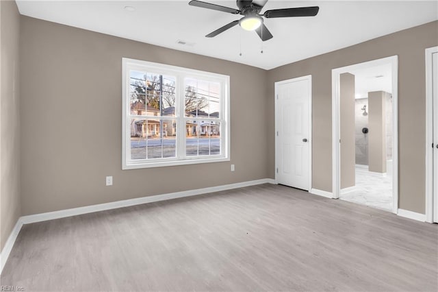 unfurnished bedroom with visible vents, wood finished floors, connected bathroom, baseboards, and ceiling fan