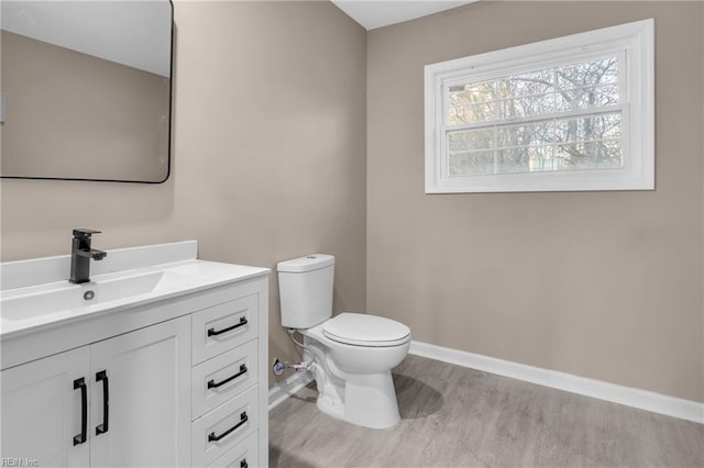 half bath with vanity, toilet, wood finished floors, and baseboards