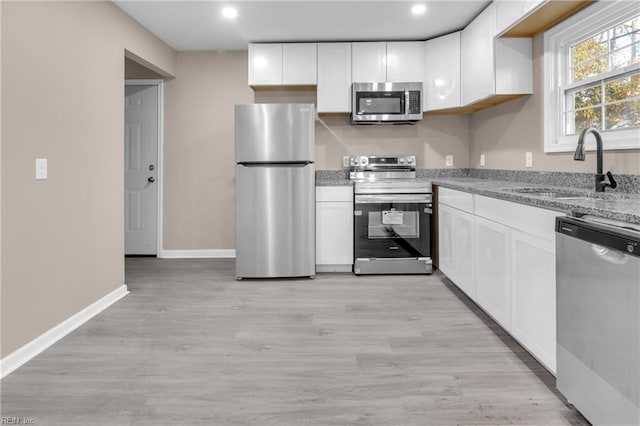 kitchen with a sink, stainless steel appliances, light wood-type flooring, and white cabinetry