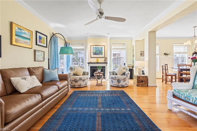 living area with ceiling fan with notable chandelier, wood finished floors, a fireplace, and crown molding