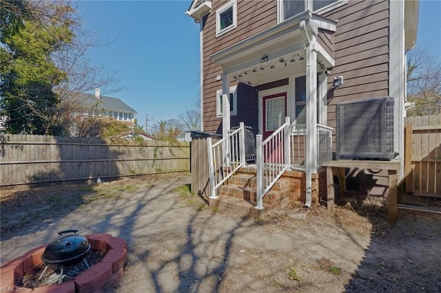 doorway to property featuring covered porch, central AC, and fence