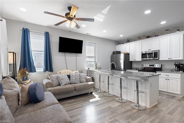 kitchen with a breakfast bar, open floor plan, light wood-style floors, appliances with stainless steel finishes, and white cabinets