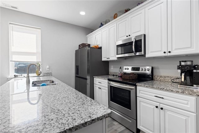 kitchen with a sink, white cabinetry, recessed lighting, stainless steel appliances, and light stone countertops