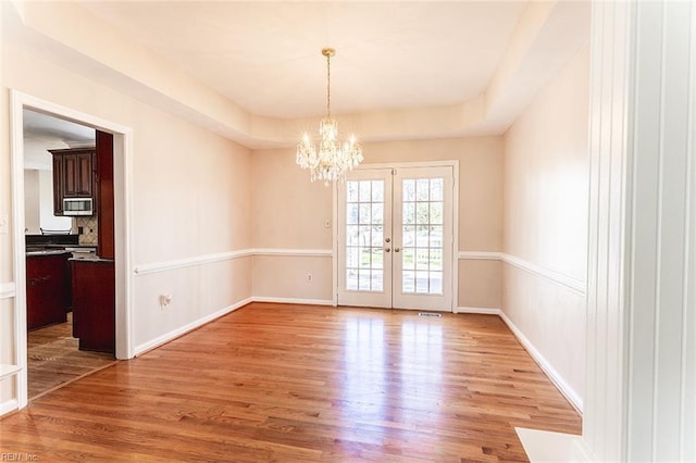 unfurnished room with a notable chandelier, baseboards, a tray ceiling, and light wood-style floors