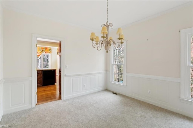 empty room featuring a healthy amount of sunlight, visible vents, carpet floors, and a chandelier