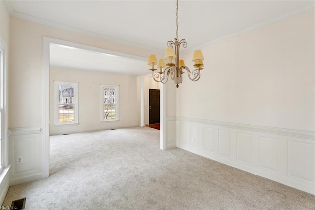 spare room with visible vents, carpet, an inviting chandelier, crown molding, and a decorative wall