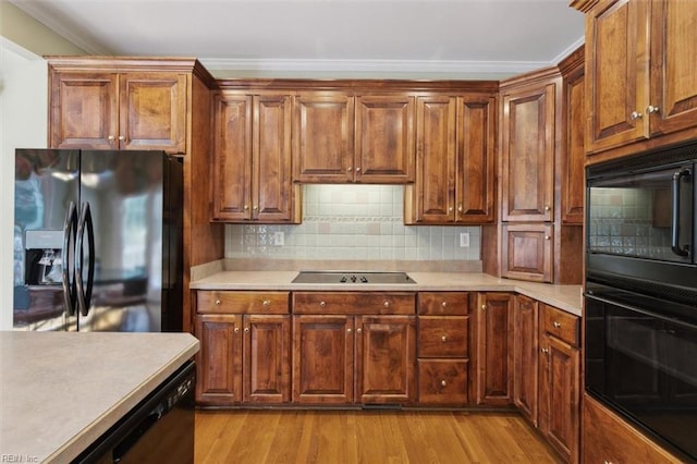 kitchen with light wood finished floors, decorative backsplash, black appliances, light countertops, and crown molding