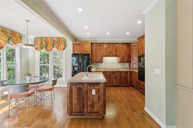 kitchen featuring black appliances, ornamental molding, light wood-style flooring, a sink, and decorative backsplash