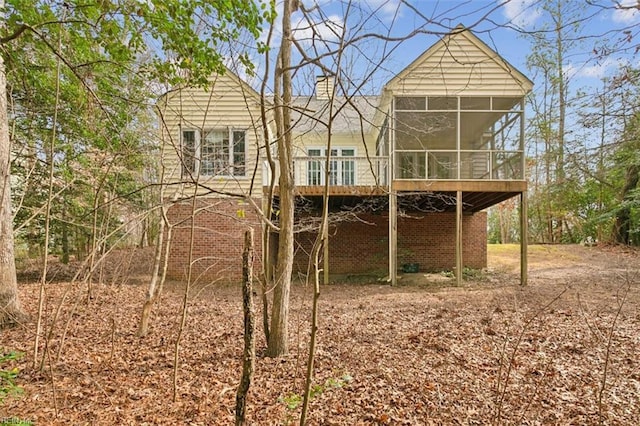 rear view of house with brick siding, a sunroom, and a chimney