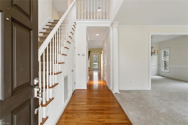 entryway featuring visible vents, stairway, light colored carpet, light wood-type flooring, and ornamental molding