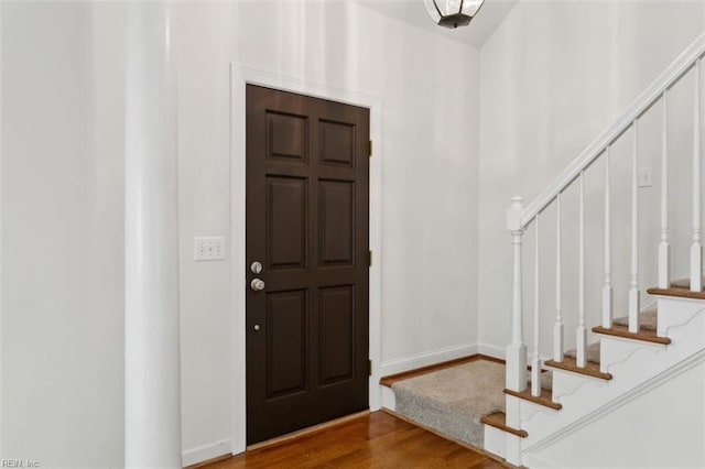 foyer featuring baseboards, wood finished floors, and stairs