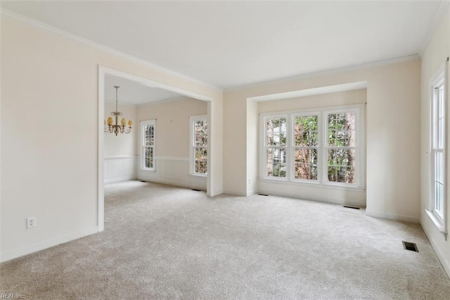 carpeted empty room featuring visible vents, a wainscoted wall, an inviting chandelier, and ornamental molding