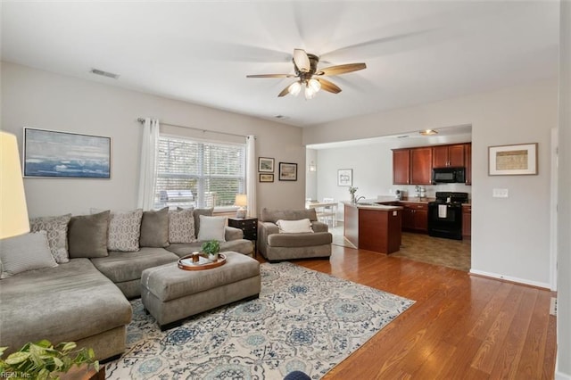 living area with baseboards, wood finished floors, visible vents, and ceiling fan