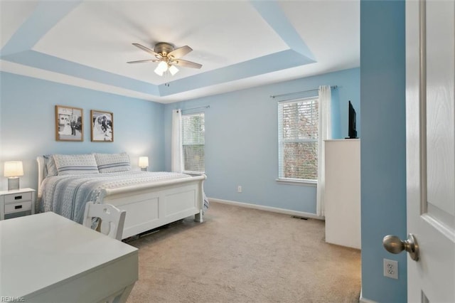 bedroom featuring a tray ceiling, a ceiling fan, baseboards, and light carpet