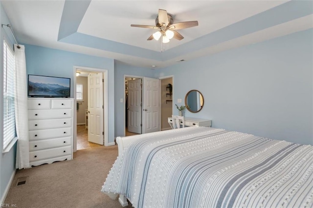 bedroom with visible vents, light colored carpet, a raised ceiling, and baseboards