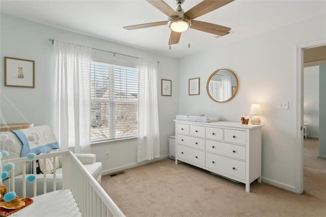 bedroom with visible vents, a crib, baseboards, light colored carpet, and ceiling fan