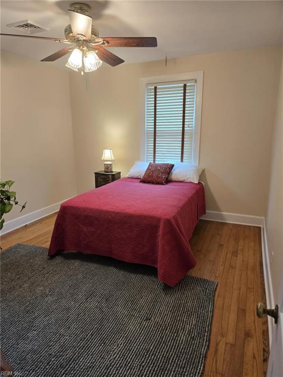 bedroom with a ceiling fan, wood finished floors, visible vents, and baseboards