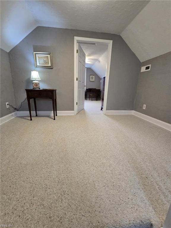 additional living space featuring a textured ceiling, visible vents, carpet, and vaulted ceiling