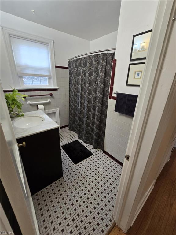 bathroom featuring a shower with shower curtain, a wainscoted wall, and tile walls