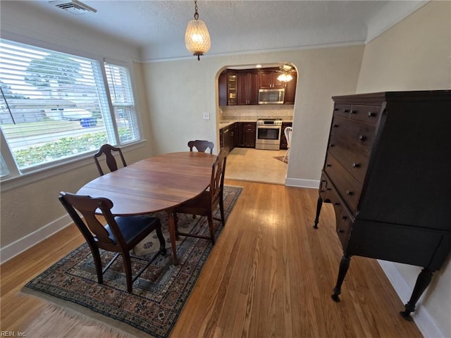 dining space featuring baseboards, visible vents, arched walkways, a textured ceiling, and light wood-type flooring