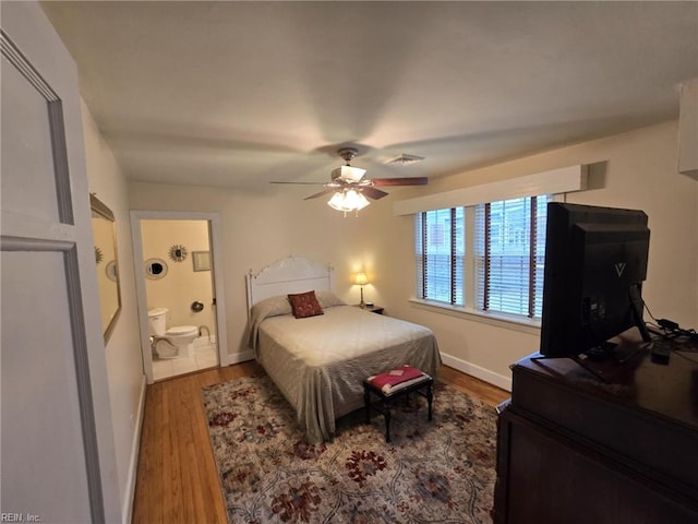 bedroom with a ceiling fan, wood finished floors, baseboards, and connected bathroom