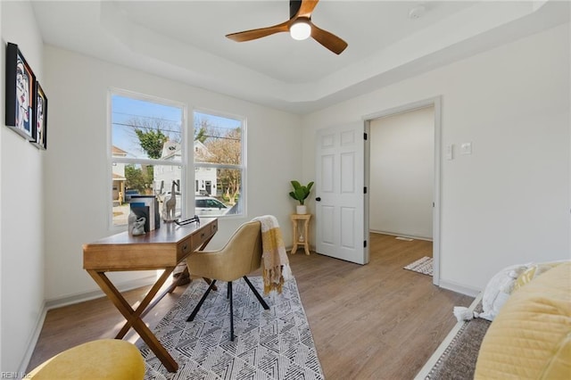 office with baseboards, a raised ceiling, light wood-style floors, and ceiling fan