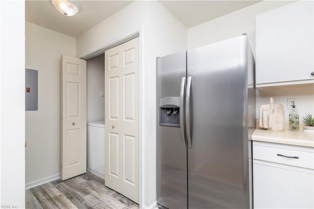 kitchen featuring stainless steel fridge with ice dispenser, light countertops, electric panel, light wood-style flooring, and white cabinetry