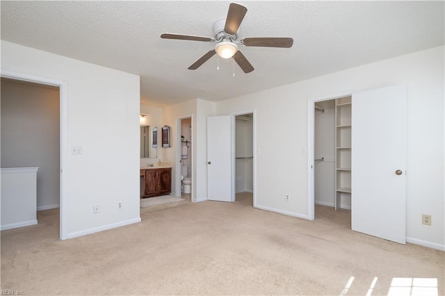 unfurnished bedroom with baseboards, a spacious closet, ensuite bathroom, a textured ceiling, and light colored carpet