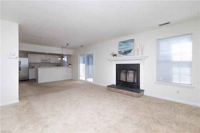 unfurnished living room with visible vents, light colored carpet, a textured ceiling, and a glass covered fireplace