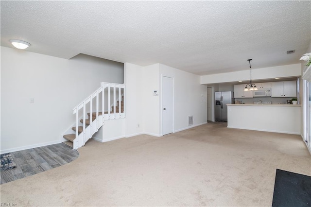 unfurnished living room with stairs, light colored carpet, baseboards, and a textured ceiling