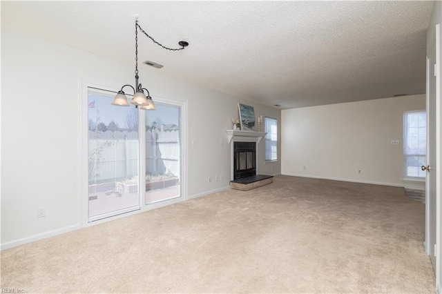 unfurnished living room with visible vents, baseboards, carpet flooring, a glass covered fireplace, and a textured ceiling