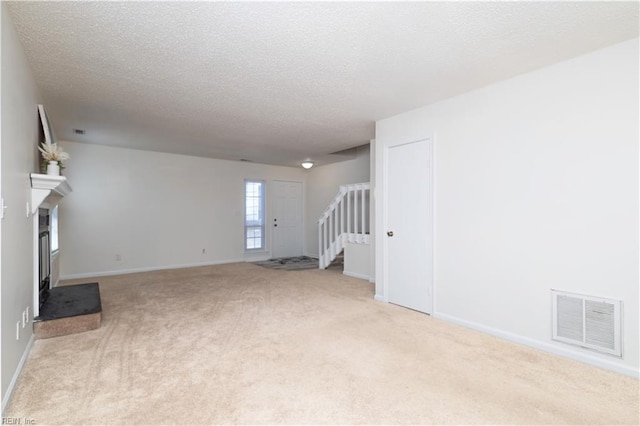 unfurnished living room with visible vents, a fireplace with raised hearth, stairway, carpet flooring, and a textured ceiling