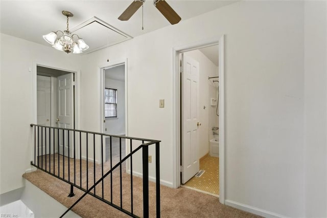 hall with an upstairs landing, attic access, baseboards, and carpet floors