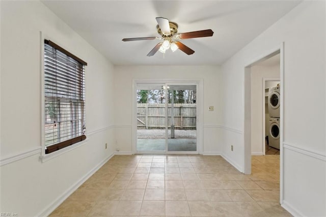 spare room featuring light tile patterned flooring, baseboards, stacked washer / drying machine, and ceiling fan