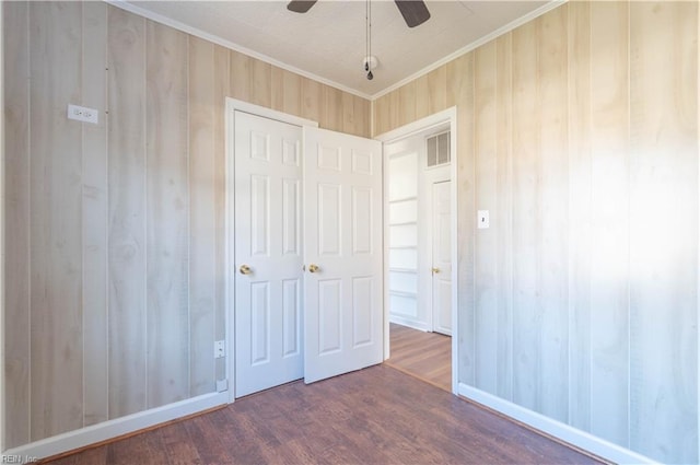 unfurnished bedroom with visible vents, ornamental molding, wood finished floors, wooden walls, and ceiling fan