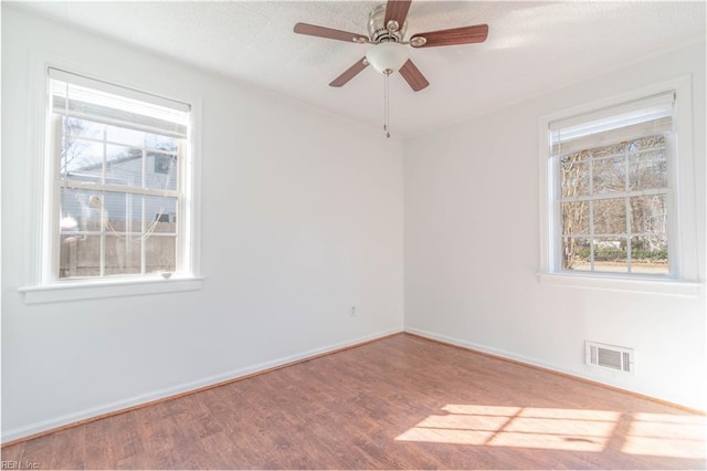 unfurnished room with a wealth of natural light, visible vents, baseboards, and wood finished floors