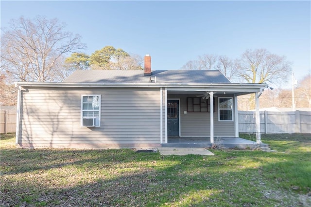 back of property featuring fence, a lawn, and a chimney