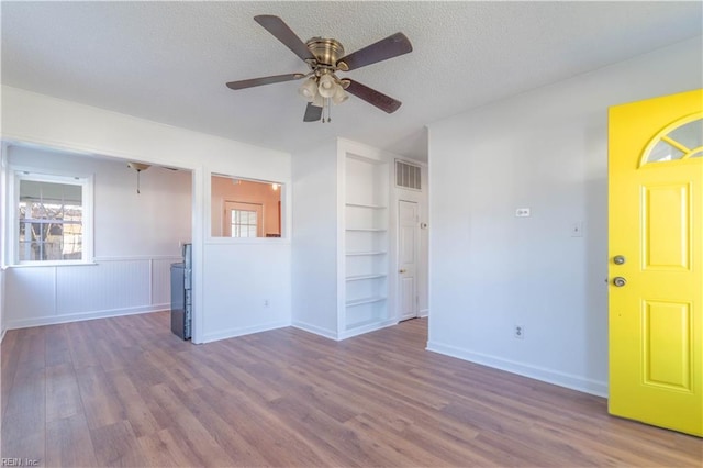 unfurnished living room with built in features, a textured ceiling, a ceiling fan, and wood finished floors