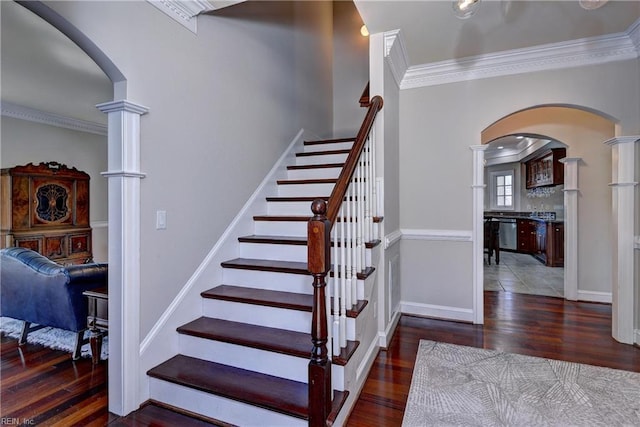 stairway with arched walkways, wood finished floors, and ornate columns