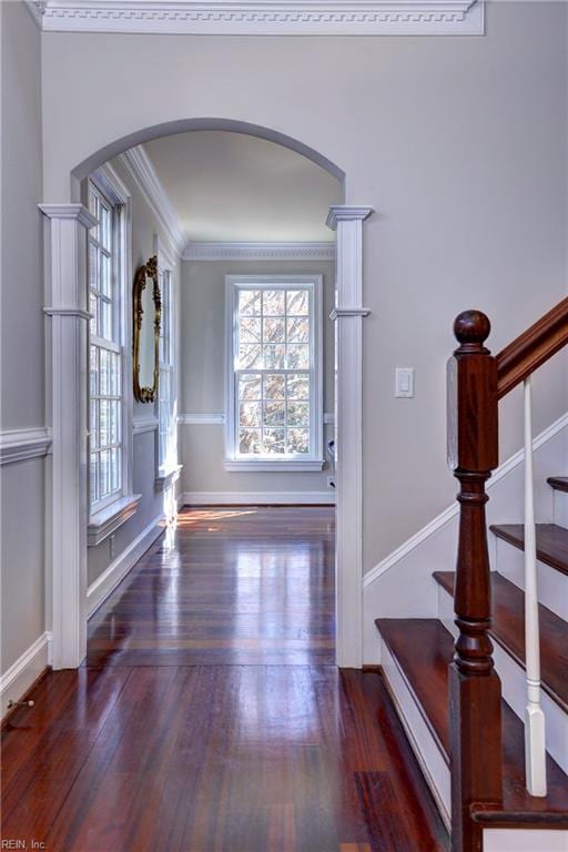 foyer featuring baseboards, stairway, ornamental molding, wood finished floors, and arched walkways