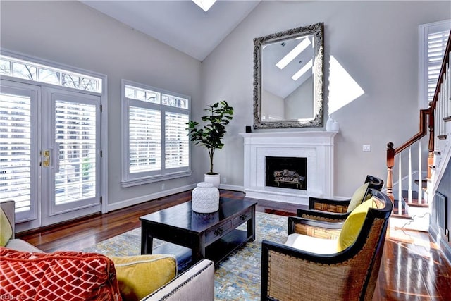 living area featuring stairway, wood finished floors, baseboards, a fireplace with raised hearth, and vaulted ceiling