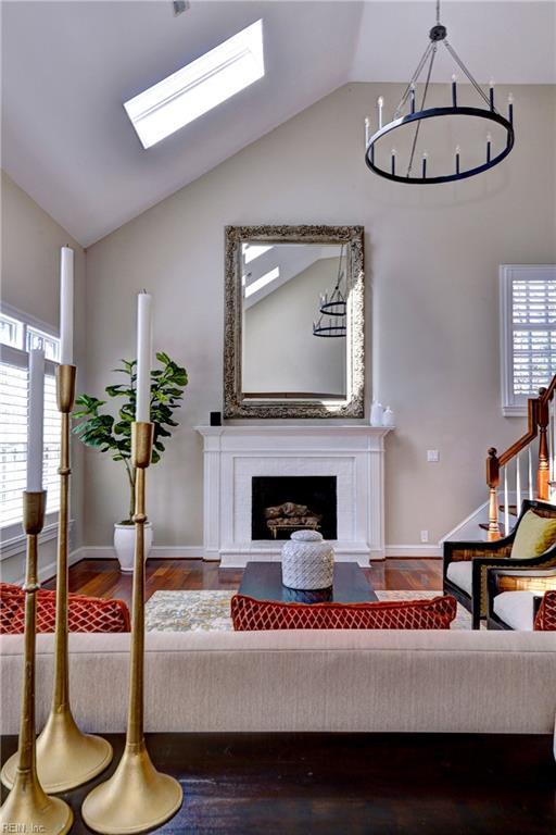 living area featuring wood finished floors, stairway, vaulted ceiling with skylight, a fireplace, and baseboards