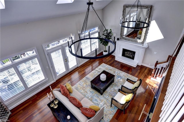 living room with plenty of natural light, a fireplace with raised hearth, an inviting chandelier, and wood finished floors