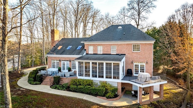 back of property featuring brick siding, a wooden deck, french doors, a chimney, and a sunroom