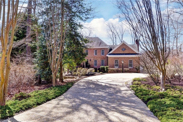 colonial house with brick siding, a chimney, and concrete driveway