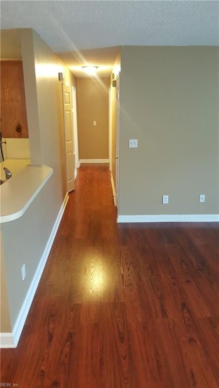 hall with baseboards, a textured ceiling, and dark wood finished floors