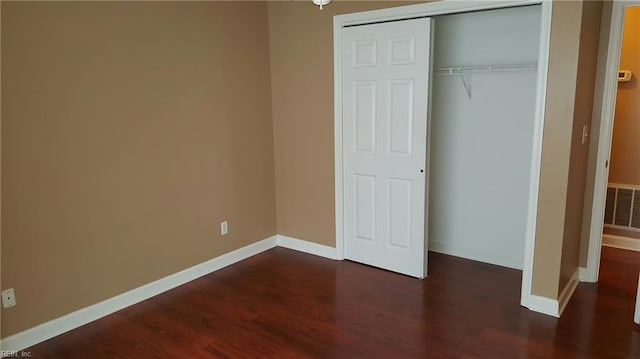 unfurnished bedroom with dark wood-type flooring, baseboards, visible vents, and a closet