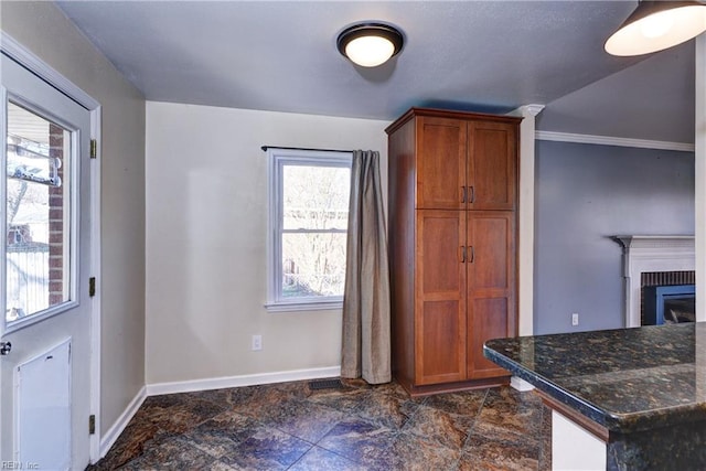 kitchen featuring dark stone countertops, a fireplace, baseboards, and brown cabinets