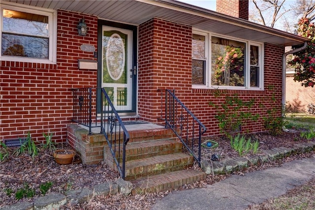 view of exterior entry with brick siding and a chimney